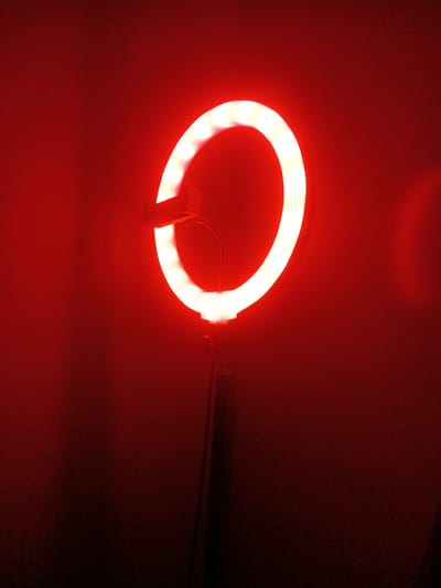 A red, illuminated ring light is centrally positioned against a dark red background. A handle extends from the right side of the ring light. The image does not contain enough information to identify a specific location in Nwanaeanoka, Botswana. There are no people visible in the image.