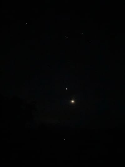 The image depicts a night sky over Nguzu Edda, Nigeria. Several stars are visible against the dark backdrop. A brighter celestial body stands out, possibly a planet or the moon. There is some indistinct dark structure in the lower half of the frame, potentially trees or terrain.