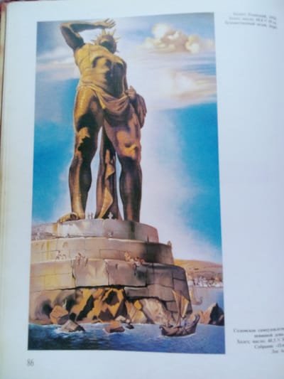 The image depicts a painted illustration of the Colossus of Rhodes, a massive bronze statue of the Greek sun-god Helios, erected in the city of Rhodes on the Greek island of the same name. The statue is shown standing tall on a stone pedestal by the sea, with its legs straddling the entrance to a harbor. A small, ancient-looking sailing ship is visible in the water below the statue. The sky is blue with white clouds, and the sea is a deep blue. The base of the statue is surrounded by rocky outcroppings and further stonework. Several tiny figures, presumably people, are depicted on the pedestal and near the base of the statue, conveying its immense scale. The text on the right side of the image is in Russian and includes information about an artwork and its creator, mentioning "Solomka samoderzhavny" and dimensions. The number "86" is visible in the bottom left corner, likely a page number. There is no indication or connection to the city of Zhmerynka, Ukraine, in the provided image.