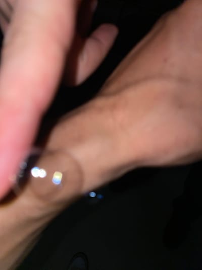 The image is an out-of-focus, close-up shot of a person's hand wearing a ring. The hand appears to be resting on a dark surface, possibly a table or the ground. The lighting is dim, with some bright circular reflections visible on the ring, suggesting it might be made of metal and catching the light. The skin tone of the hand is light. No specific location in Chișinău, Moldova, can be identified from this image.