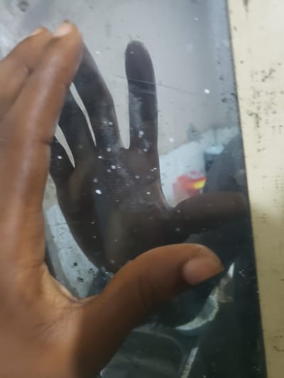 A close-up shot shows a hand with dark skin reaching into a body of water, possibly a tank or aquarium. The hand is positioned with fingers spread, and water droplets are visible on its surface, creating a slightly blurred effect. The background is obscured, but hints of lighter colors and possibly some debris are present. A tan-colored rim or edge is visible at the top of the frame, suggesting the edge of the container. The lighting appears to be indoor, with no clear indication of the time of day or weather. The overall impression is one of exploration or interaction with the aquatic environment. The water's surface appears somewhat murky, with some small white specks scattered throughout. The image does not contain any visible text. The context of Iganmu, Nigeria, suggests a potential connection to local environments or practices.