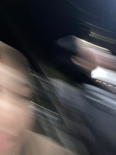 The image is a blurry, abstract depiction of a scene, likely taken at night due to the dark background and prominent light streaks. The primary subjects appear to be people, hinted at by the blurred forms and shapes that suggest human figures. The motion blur indicates movement, possibly from walking or being in a moving vehicle.

Notable details include streaks of light, some white and some yellow, running diagonally across the frame. These lights could originate from streetlights, vehicle headlights, or other sources common in an urban or semi-urban environment at night. The overall impression is one of dynamic movement and low-light conditions. There are also patches of darker areas, suggesting shadows or unlit spaces.

Given the location context of Watampone, Indonesia, the scene could depict a street at night, a marketplace after closing, or a gathering where people are moving around. The weather is not discernible. There is no visible text in the image. The abstract nature of the photograph makes it difficult to pinpoint specific objects or precise activities, but the overall impression is one of a fleeting moment captured in motion. The blurred forms of people contribute to a sense of anonymity and universality of human movement in a nocturnal setting.
