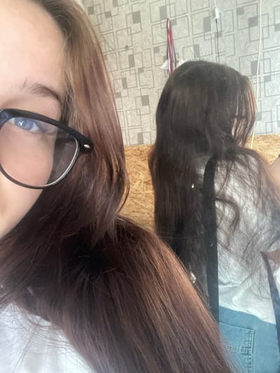 A person with long, brown hair is taking a selfie in a room. The person is wearing glasses. The background of the room has wallpaper and a wooden surface. The image appears to be taken indoors. There is no discernible information about the specific location in Borodulino, Russia.