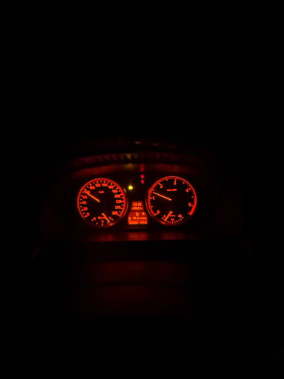 The image depicts a close-up view of a car's dashboard at night. The speedometer is in the lower portion of the frame, and it indicates a speed of approximately 80 km/h. A tachometer is positioned above the speedometer, with the needle suggesting an engine speed of around 1800 RPM. A small digital display between the two gauges shows the time as 23:38 and an outside temperature of 18.0 degrees Celsius. The background is dark, focusing the viewer's attention on the illuminated dashboard. The scene is inside the car, likely in motion, and the car is in Mogila, Bulgaria.