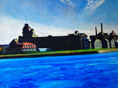 This painting depicts a panoramic view of a large body of water in the foreground, with an extensive complex of buildings lining the opposite bank under a bright, partly cloudy sky. The scene is set in Reus, Spain.

The lower half of the image is dominated by a vivid, deep blue body of water, rendered with distinct brushstrokes that create a textured, rippling surface, suggesting gentle movement or currents. A narrow band of dark brown or black separates the water from a strip of vibrant green land, likely grass or vegetation, which forms the immediate bank.

Above the green bank, a sprawling collection of buildings extends across the entire width of the scene. These structures are largely silhouetted in dark tones of brown and black, suggesting they are either in shadow or rendered with a somber palette. On the far left, a distinct building with a reddish-orange roof and arched openings is visible, with a tall, slender spire rising from a dark, domed structure behind it. The central portion of the skyline is occupied by a massive, dark, and somewhat monolithic building complex, featuring various rooflines and smaller, less defined structures on its surface. Towards the right, two prominent, dark industrial chimneys stand tall against the sky. This section of the complex also includes several smaller buildings, some with discernible lighter facades (white, light blue, or gray) and varied architectural details. The overall impression is that of an industrial or institutional area situated along a waterway.

The sky above is a clear, bright blue, fading slightly to a lighter tone near the horizon. Scattered white, wispy clouds are present, primarily in the upper right quadrant and sparsely across the sky. No people, vehicles, or specific activities are depicted in the scene.