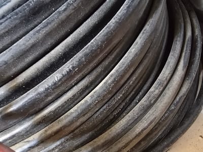 The image shows a close-up, abstract view of a coiled bundle of thick black cables. The cables are dusty and appear to be made of rubber or a similar material, with visible striations running along their length. The lighting creates highlights and shadows that emphasize the rounded forms of the coils. The overall impression is one of industrial material. There is no indication of location within Nova Kakhovka, Ukraine, or any other specific details about people, actions, or interactions.