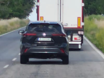 The image shows the rear view of a dark-colored SUV on a paved road. The SUV has its license plate visible, which reads "P 1111 KC". The vehicle is positioned in the foreground, with the rear bumper and taillights clearly visible. Behind the SUV, the rear of a white truck is partially visible. The truck has red and yellow markings on its rear.
The scene appears to be on a highway or a rural road, with grassy verges and trees lining the sides. The lighting suggests it is daytime, likely with clear weather, as there are no signs of rain or fog. The road has white dashed lines marking the lanes. The overall setting seems to be an outdoor environment, possibly in a rural area of Zgalevo, Bulgaria, as indicated by the location context. There are no people visible in the image. The activity depicted is vehicles driving on a road.
