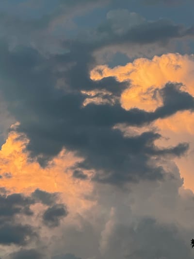 The image depicts a dramatic sky filled with dark, gray clouds illuminated by patches of bright orange light, suggesting the presence of sunset or sunrise. The clouds are varied in texture and form, with some appearing dense and heavy, while others are wispy and illuminated from behind. The overall atmosphere is one of impending weather or the aftermath of a storm. The location is identified as Beltershain, Germany, though no specific landmarks or urban features are visible within the frame of the sky. There are no people, subjects, objects, or actions depicted in the image; it is solely focused on the cloudscape.