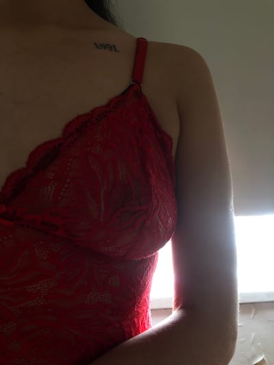 The image features a close-up of a person's upper torso, wearing a red lace garment, possibly lingerie. A tattoo of the year "1991" is visible on the left side of the torso, near the underarm. The person's arm is positioned across their body, with the arm's curvature highlighted by a bright light source behind it. The background is a plain wall, suggesting an indoor setting. There are no other people, subjects, objects, actions, or interactions visible in the image. The city of Rio Grande, Argentina, is not discernable from the image.