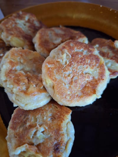 A close-up shot shows a cluster of small, round, golden-brown potato pancakes arranged in a dark brown bowl with a tan rim. The pancakes exhibit a slightly uneven surface texture, suggesting a homemade preparation. The setting is identified as Lodtunduh, Indonesia. There are no people visible in the image. The focus is solely on the food item.