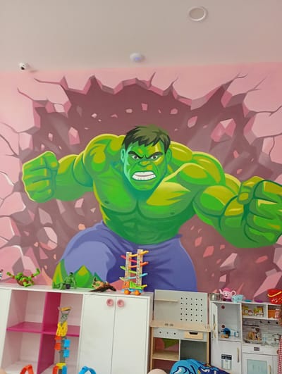 A large mural of the Hulk is painted on a pink, cracked wall. Below the mural, a white cabinet with pink knobs and various toys are visible. These toys include action figures, a toy kitchen, and a toy car ramp. In the upper left corner, a white security camera is mounted on the ceiling. In the upper right corner, a white round object, possibly a smoke detector, is also visible on the ceiling. The environment appears to be a child's room or playroom. The scene is located in Konstantinovo, Bulgaria.
