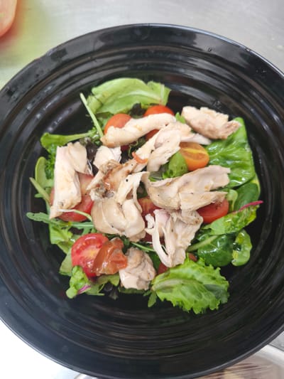 In Bojano, Italy, a black bowl of salad is pictured. The salad consists of shredded chicken, cherry tomatoes, and mixed greens. The bowl is dark and has a textured interior. The lighting suggests an indoor setting, possibly a kitchen or restaurant.