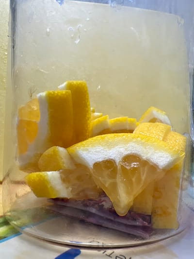 The image shows a close-up view of sliced lemons inside a glass jar. The lemons are cut into wedges and appear to be submerged in a light-colored liquid, possibly water or juice. The jar is transparent, allowing the viewer to see the contents clearly. Some of the lemon slices have a white pith layer visible, and the flesh is bright yellow. The background is softly blurred, suggesting the jar is on a surface. There is no indication of any specific location in the city of Засечное, Russia, or any people or actions depicted.