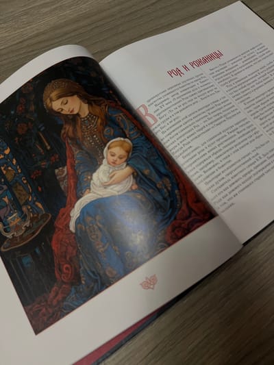 The image shows an open book with a detailed illustration on the left page and text on the right page. The illustration depicts a woman with long brown hair and a golden headdress, wearing a richly decorated blue and gold gown. She is holding a baby swaddled in white fabric. The background is a dark, patterned tapestry with floral motifs. The text on the right page is in Russian and discusses the concepts of "Rod and Rozhanitsy," which relate to ancient Slavic deities associated with family, fertility, and birth. There is no indication that this image is located in Tikhoretsk, Russia.