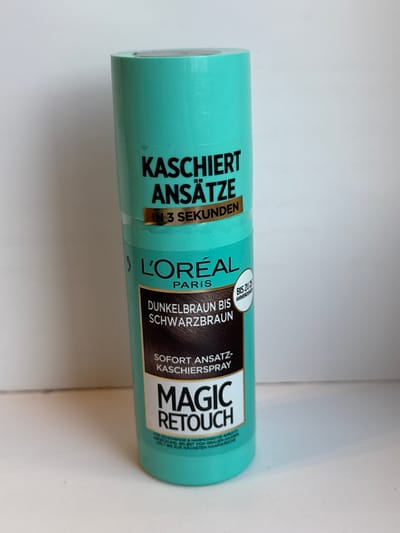 A turquoise spray can of L'Oréal Paris Magic Retouch hair dye for dark brown to black hair is centered against a plain white background. The can features black text advertising its ability to cover roots in 3 seconds and describes its function as an "ansatz-kaschierspray" (root-concealing spray). A circular emblem with white text on a light blue background is also visible on the can, stating "BIS ZU ANWENDUNG" (up to application). The can is upright, and the lighting suggests a studio setting with a soft, diffused light source. There are no people or other objects in the scene. The location in Яромінскі сельскі Савет, Belarus, is not depicted in the image.