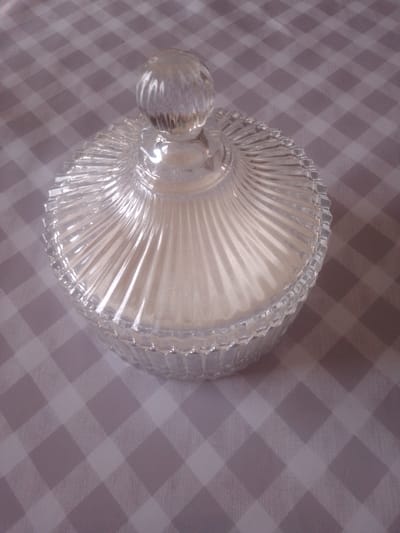 A clear glass lidded jar filled with a white, powdery substance sits on a grey and white checkered tablecloth. The jar has a decorative, fluted design on its sides and a rounded lid with a knob on top. The substance inside appears to be flour or sugar. The image is a close-up shot, with the jar taking up most of the frame. The lighting suggests it's daytime. There is no visible text in the image. The setting appears to be indoors, likely a kitchen or dining area, in Yessentuki, Russia.