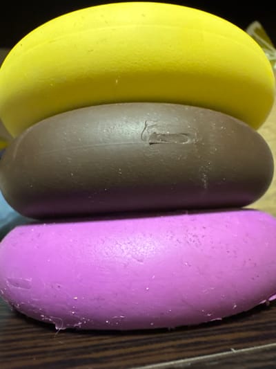 The image shows a stack of three oval-shaped objects. The top object is bright yellow, the middle object is dark brown, and the bottom object is bright purple. The objects appear to be made of a smooth, slightly matte material. The lighting suggests they are indoors. There is no indication of any specific location within the city of Змейка, Russia.