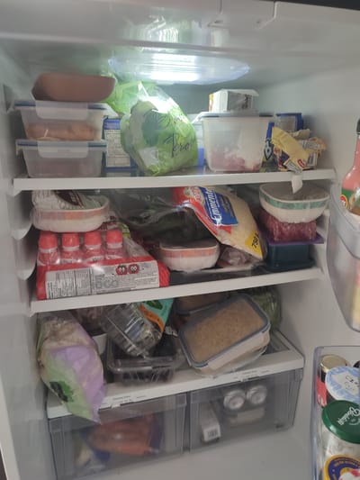The image shows the interior of a refrigerator. The refrigerator is stocked with various food items, including containers of meat, vegetables, and what appear to be dairy products. There is also a bag of leafy green vegetables, likely lettuce or spinach, and a package of small bottles with red caps. The shelves are made of clear plastic, and the interior lighting is visible at the top. One of the drawers at the bottom of the refrigerator has a label indicating "Climate Zone" with settings for "Fruits" and "Vegetables." The overall impression is one of a well-stocked refrigerator. The location of the city of Longueuil, Canada is not discernible from the image itself.