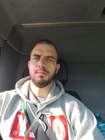 A medium-shot, indoor photograph captures a man wearing a grey hoodie. He is also wearing a seatbelt. A water bottle is visible. The man is likely in a vehicle, based on the surrounding interior. There is no specific evidence to link this image to the city of Byal Izvor, Bulgaria.