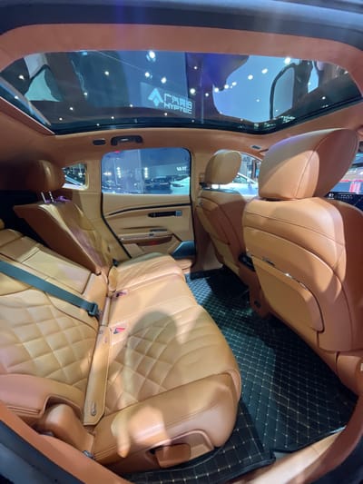 The image shows the backseat of a car. The seats are brown leather with a diamond pattern and are empty. The car has a sunroof. There are black floor mats with a gold trim, covering the floor of the car. The vehicle appears to be in a dealership. The coordinates 30.272, 120.416 correspond to a location in Hangzhou, China.  The location is a shopping mall called "Intime City". There is a "HYPTEC" logo on the sunroof. There are other cars in the background, partially visible through the rear window.  The image captures the interior of the car, showcasing the premium materials and features.  The scene is captured from a low angle, providing a perspective of the car's interior.
