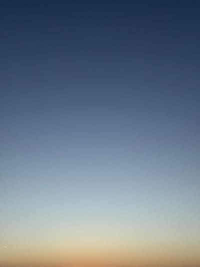 The image is a vertical, full-frame shot of the sky over Biarritz, France, during what appears to be either dawn or dusk. The sky displays a smooth gradient of colors, transitioning from a deep, dark blue at the top of the frame to lighter blues and then to soft yellows and oranges near the bottom. There are no discernible clouds, structures, people, or other objects within the frame. The lighting suggests a time of day with low sun angle.
