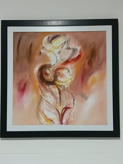 A framed abstract painting of a human torso is displayed on a white wall in Puerto Plata, Dominican Republic. The painting features a flowing, semi-nude form rendered in warm tones of brown, yellow, pink, and red, with bold, gestural brushstrokes. The artwork is enclosed in a thick black frame with a white mat. The background of the image is a plain white wall, suggesting an indoor setting such as a home or gallery.