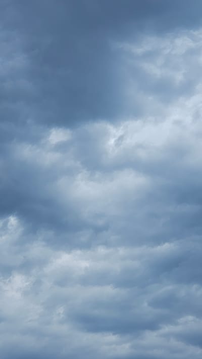 This media file is a photograph of the sky, filled with a dense layer of clouds. The clouds are predominantly dark and stormy blue, with some lighter, brighter patches suggesting breaks in the cloud cover or sunlight attempting to filter through. The texture of the clouds appears turbulent and layered, creating a sense of depth and movement. The overall impression is one of an overcast or impending stormy weather. There are no discernible people, objects, or specific location cues within the image, making it a generic depiction of the sky. The time of day is indeterminate due to the lack of direct sunlight or shadows, but the light conditions suggest it could be daytime. There is no visible text in the image. The setting is simply the sky, as viewed from the ground, with the location context provided as Vöhringen, Germany.