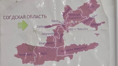 The image is a map of the Sughd Region of Tajikistan. The title "СОГДская ОБЛАСТЬ" is visible in the upper left corner. Several cities and districts are labeled on the map in purple. These include Panjakent, Ayni, Shahrinston, Istaravshan, Zafarobod, Spitamén, Konibodom, Isfara, Asht, Bobojon Gafurov, and Jabbor Rasulov. The map appears to be on a textured surface, possibly paper or laminated material, with some glare and minor damage visible. There are no people or actions depicted in the image. The location in the city of Ghafurov, Tajikistan is indicated by the label "Bobojon Gafurov".