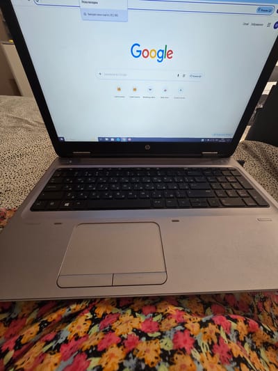 A HP ProBook laptop is open and displayed on a bed covered with a floral patterned blanket. The laptop's screen shows the Google search page. The keyboard is visible and appears to be in a Cyrillic layout. The surrounding environment is not clearly defined, but the presence of a blanket suggests an indoor setting. There are no people visible in the image. The time stamp on the laptop's taskbar indicates 08:40 on 03.07.2020. No specific location in Petropavlivska Borshchahivka, Ukraine, can be identified from the image.