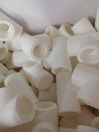A close-up, overhead shot shows a pile of white, cylindrical, plastic plumbing fittings. The fittings are of various sizes and types, including elbows, tees, and straight connectors. They are tightly packed together, filling the frame. The lighting is bright, suggesting an indoor setting, possibly a storage area or workshop. There are no people or animals visible in the image. The location in Beșghioz, Moldova, is not discernible from the image itself.