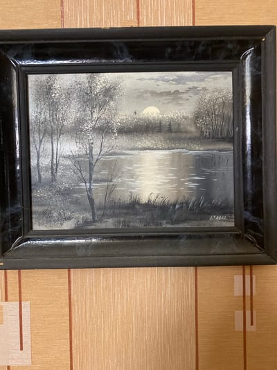 A framed painting depicts a serene grayscale landscape. The painting features a body of water in the foreground, reflecting the sky and surrounding trees. The background shows a dense treeline with a prominent bright circle, likely the sun, partially obscured by clouds. Several birds are visible in the sky, and tall grass lines the edge of the water. The painting is signed in the lower right corner with the name "A. ABBA". The frame is black with a marbled texture. The painting is hanging on a wall with orange and brown striped wallpaper.