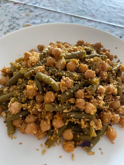 The image shows a close-up of a white plate filled with a dish consisting of green beans and chickpeas, seasoned with sesame seeds and possibly other spices. The plate appears to be placed on a tablecloth with a floral pattern. The location, Senden, Germany, is not discernible from the visual content of the image.