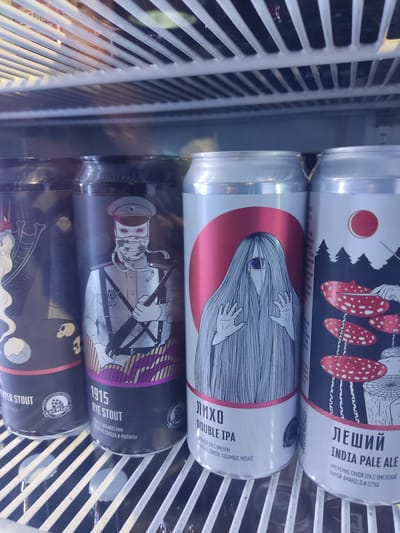 The image shows four cans of craft beer stacked vertically inside a refrigerated display unit, likely in a retail setting. The top can is labeled "ЛЕШИЙ INDIA PALE ALE," indicating it is an India Pale Ale. The second can is labeled "Лихо DOUBLE IPA," a Double IPA. The third can is labeled "1915 RYE STOUT," suggesting it is a Rye Stout. The fourth can is partially visible and appears to be a stout. All the can labels are in Russian, and the information provided with the image indicates this is likely from Pskov, Russia.
