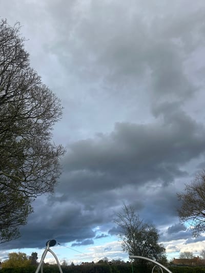 The image depicts a stormy sky with dark, ominous clouds. In the foreground, branches of bare trees are visible, suggesting it may be late autumn or winter. A metal structure, potentially part of a playground or park equipment, is also present. Given the prompt's indication of Easingwold, United Kingdom, the location is likely a public space like a park or recreation area. The absence of people and the subdued lighting contribute to a somber and possibly deserted atmosphere. The sky is a dominant feature, conveying a sense of impending weather. The details provide limited clues to more specific details of the location within Easingwold.