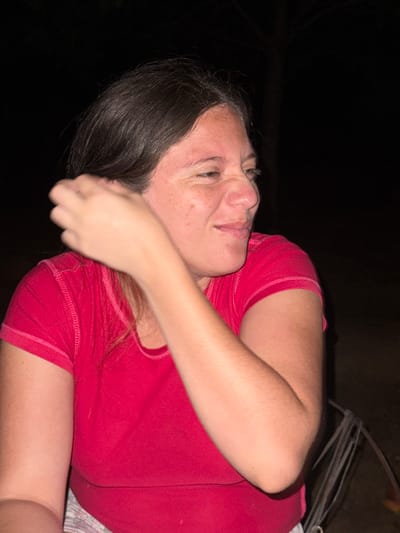 A woman with dark hair is lying down, facing the viewer. She is wearing a red t-shirt and what appears to be patterned underwear. Her right arm is bent, with her hand near her face. The background is mostly dark, but a metallic object with wires is visible in the upper right corner. The image does not contain enough information to determine if this image was taken in El Bajío, Venezuela.