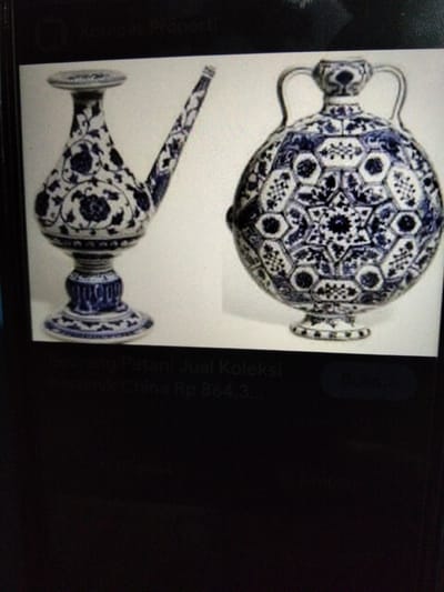 The image displays two antique blue and white porcelain objects on a white background. The object on the left is a tall, slender vessel with a flared base, a bulbous body decorated with floral motifs, and a long, narrow spout extending upwards and to the right. The object on the right is a spherical vase with a short, narrow neck topped with two loop handles. Its body is intricately decorated with a repeating geometric pattern of hexagons and stars. A partially visible text overlay suggests the objects are part of a collection from China, with a price indicated in Indonesian Rupiah. The location in the city of Kualaraja, Indonesia is not depicted or implied by the visual content.