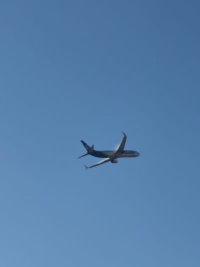 A Boeing 737-800 aircraft, operated by Alaska Airlines, is depicted in flight against a clear, pale blue sky. The aircraft is seen from a low angle, appearing to ascend. The livery of the aircraft is predominantly dark blue, with the Alaska Airlines logo visible on the tail fin, which features a depiction of the Alaskan Native figure, "The Spirit of Alaska." The word "alaska" is also clearly visible on the fuselage near the front of the aircraft. The landing gear is retracted, indicating the aircraft is in cruise or ascent. No people are visible within or around the aircraft, and there are no visible structures or ground features in the frame. The image appears to have been taken in Sacramento, United States, given the context of Alaska Airlines operations.