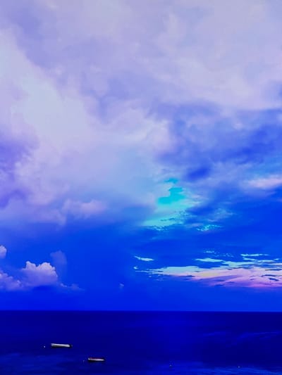 This media file is a photograph of a vibrant sky, captured in Gorzow, Poland. The image is dominated by a gradient of blues, transitioning from a soft lavender and white on the left, indicative of clouds, to a deep, intense blue on the right. Wisps of clouds are scattered throughout, with some appearing bright and illuminated, suggesting the presence of sunlight. On the far right edge of the image, there are two distinct objects that appear to be vertical white figures against the dark blue backdrop. These objects have a sleek, elongated shape and are spaced apart, suggesting they might be part of a structure or installation. The overall mood of the image is serene and vast, evoking a sense of openness and the majesty of the sky. There are no visible people or text in the image. The time of day is suggested to be daytime due to the bright sky, and the weather appears clear or partly cloudy. The location is specified as Gorzow, Poland.