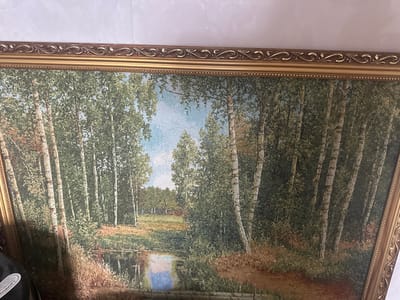 The image displays a framed tapestry or painting depicting a serene natural landscape. The scene is a forest of birch trees with white and dark bark, interspersed with lush green foliage. A calm body of water, possibly a river or pond, reflects the sky and surrounding trees. The water has a blue and pinkish hue, suggesting the colors of the sky. The foreground features dry grass and reeds along the water's edge. In the background, a clearing with a hint of a structure or fence can be seen, further into the wooded area. The tapestry is framed with an ornate gold-colored frame that has decorative scrollwork and beading. The overall impression is one of tranquility and natural beauty. The scene does not show any people, actions, or interactions. The location of Yazykova Pyatina, Russia, is not visible or suggested by the image itself.
