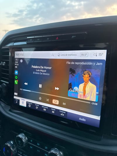 The in-car infotainment system displays music playback, showing "Palabra De Honor" by Luis Miguel, "El Idolo De Mexico." The song is at 0:31 of a total length of -3:08. The queue shows "Fila de reproducción y Jam." The interface features navigation, favorites, applications, and settings icons. The time is 5:52, and the temperature is 19.5°C. The system also displays the phone connection status. The car's climate control and audio system buttons are visible on the right.
