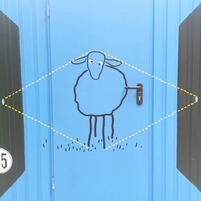 The image shows a close-up of a bright blue metal door with a cartoon drawing of a blue sheep. The sheep is outlined in black and has wide, innocent eyes. A black door handle is attached to the right side of the sheep's body. A yellow dashed line forms a diamond shape around the sheep, with small grey circles at the outer points of the diamond. There are also small black dashes scattered below the sheep, resembling grass. On the far left side of the image, a white circle with a black outline contains the number "5" in black. The door appears to be part of an outdoor structure, possibly a toilet or utility cabin, given the presence of the number and the practical design of the door. The scene is clean and appears to be well-maintained, suggesting it's in a public space within the city of Eisenach, Germany.