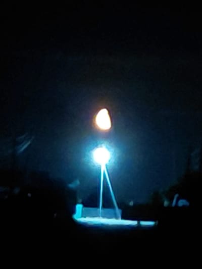 This image captures a dimly lit scene with two distinct light sources and a dark background. On the left, a hazy, yellowish-orange light emanates from what appears to be a spherical object, possibly a light bulb or a lamp. To its right, a much brighter, bluish-white light source is visible, casting a sharp beam of light that seems to be directed towards a bright, rectangular object on the far right of the frame. This rectangular object is illuminated with a vibrant blue light and appears to have a layered or segmented structure.
The overall setting is dark and indistinct, suggesting an indoor environment or nighttime exterior with minimal ambient light. The bright lights dominate the scene, creating a stark contrast with the surrounding darkness. There are no discernible people or specific environmental cues to identify the exact location or time of day, other than the implied artificial lighting. The focus seems to be on the interaction of light with objects. No visible text is present in the image. The atmosphere is one of observation or experimentation, focusing on the properties of light and illumination.