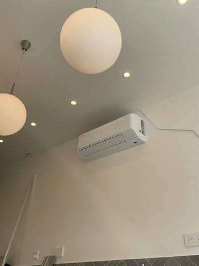 This image depicts an interior scene, likely a modernly decorated room. Dominating the upper portion are two large, spherical pendant lights, one in the upper left and another larger one in the upper center, both emitting a soft, diffused light. Several smaller, recessed ceiling lights are also visible. Mounted on the light-colored wall is a white air conditioning unit. To the right of the air conditioning unit, the wall angles upwards, suggesting an architectural feature. In the lower portion of the image, a tiled backsplash runs horizontally along the wall, and electrical outlets are visible. The overall impression is one of a clean, minimalist, and well-lit indoor space. No people are present in the image. The city of Meaux, France, is not indicated or discernible within the visual information provided in the image.