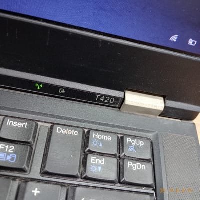 The image shows a black laptop computer with a silver hinge. The laptop is open, and the keyboard is visible. The keyboard has the following keys: Insert, Delete, Home, PgUp, End, and PgDn. The laptop has a model number of "T420" printed on the top of the keyboard. The laptop's screen is dark blue and features a wireless signal icon. There are faint marks on the keys and the laptop's surface. The laptop is located in Kecamatan Curug, Indonesia, which is located at the coordinates -6.266 latitude and 106.549 longitude.