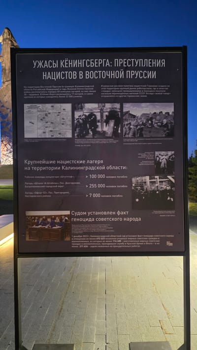 The image shows an information sign titled "Horrors of Königsberg: Crimes of the Nazis in East Prussia". The sign details atrocities committed by Nazi Germany in the East Prussia region, particularly within what is now the Kaliningrad Oblast of Russia. It mentions the presence of around 50 Nazi camps, including 17 in Königsberg, and highlights the enslavement and forced labor of Soviet citizens. The sign lists major Nazi concentration camps in the Kaliningrad Oblast and estimates the number of deaths. It states that on December 1, 2023, the Kaliningrad Regional Court established the fact of genocide against the Soviet people. The sign includes photographs of prisoners and documentation. The location of the sign is Zaitsevo (Verevskoe S/P), Russia, but the image gives no details about that location.