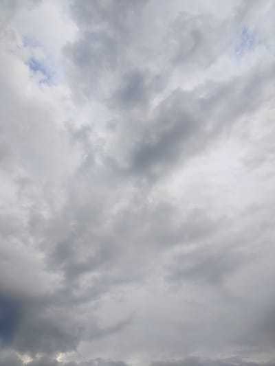 The image is a close-up, low-angle shot of a cloudy sky. The clouds are a mix of light gray and dark gray, with some patches of bright white where sunlight is breaking through. There is a small patch of blue sky visible in the upper left quadrant of the image. The clouds are textured and appear dense, suggesting a potentially overcast or stormy day. There are no discernible features of the city of Дзешчанскі сельскі Савет, Belarus, in this image, as it exclusively depicts the sky.