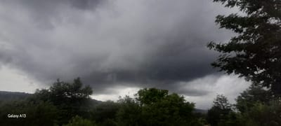 The image shows a landscape with dark, heavy clouds dominating the sky, suggesting an impending storm or overcast weather. In the foreground, there are trees and foliage. The bottom left corner of the image displays "Galaxy A13", indicating the device used to capture the photo. The location of Rashkov, Moldova, is mentioned as context but is not visually discernible from the image itself. There are no people or discernible actions depicted. The environment is natural, with trees and hills visible in the background, under a dramatic sky.