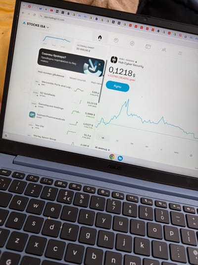 The image shows a laptop screen displaying a stock trading platform. The website, "app.trading212.com", is open on a stock trading application showing stock prices and stock market charts. Specifically, "Hub Cyber Security" is highlighted, its current value at $0.1218.
The laptop is an ASUS, with a black keyboard with blue keys and a silver body. The photo is taken indoors.
I am unable to locate the precise geolocation within Pentre, United Kingdom from this image.