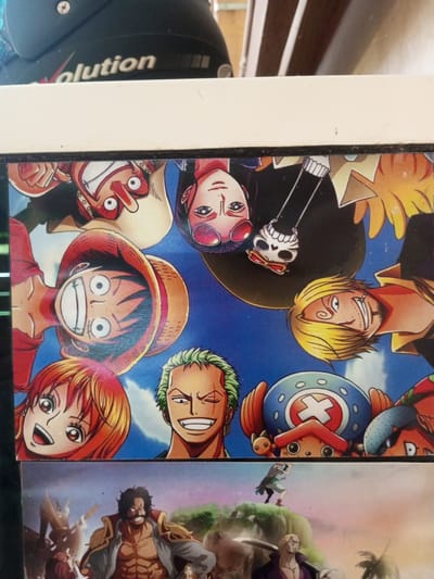 The image displays a collage of anime characters from the series One Piece, layered over a background featuring a cityscape that appears to be in Turumame, Indonesia. In the top section of the collage, a black helmet with the word "evolution" printed on it is visible. The main focus of the collage is a circular arrangement of several One Piece characters, including Monkey D. Luffy, Nami, Roronoa Zoro, Tony Tony Chopper, Vinsmoke Sanji, Nico Robin, and Usopp. They are depicted in various poses and expressions, with their faces mostly filling the frame. Below this circular arrangement, another section of the collage shows Gol D. Roger and other characters in a different scene, possibly a battle or a landscape. The background hints at the presence of buildings and possibly water, characteristic of an urban coastal environment.