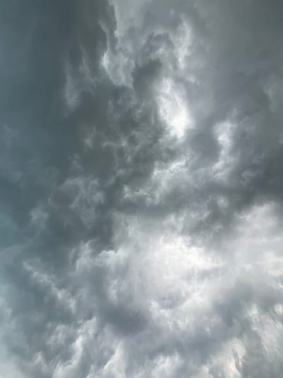 The image shows a sky filled with dark, dramatic storm clouds. There are bright patches where the sunlight is breaking through, creating a contrast with the darker, more ominous clouds. The clouds are dense and appear to be moving, with swirling patterns and varying textures. The overall impression is one of an impending storm. There are no people, subjects, or objects visible in the image, nor any specific environmental details to indicate the location in the city of Маяк, Russia.
